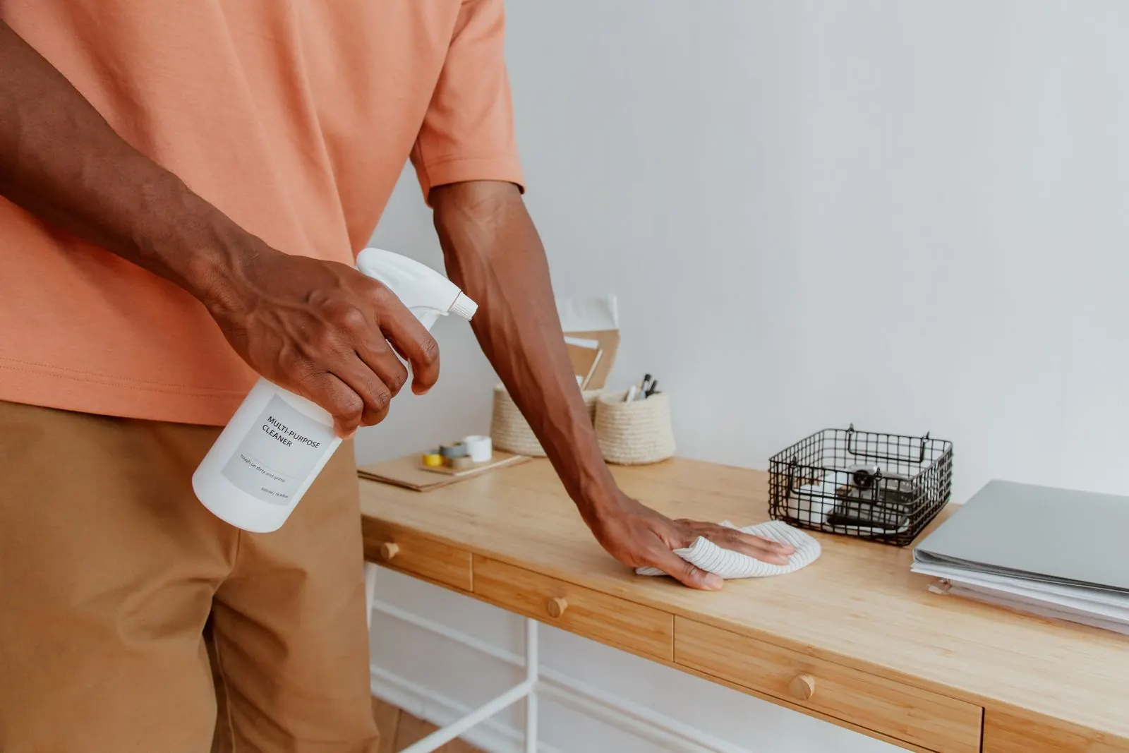 Janitorial cleaner wiping down an office desk with a microfiber cloth and spray bottle
