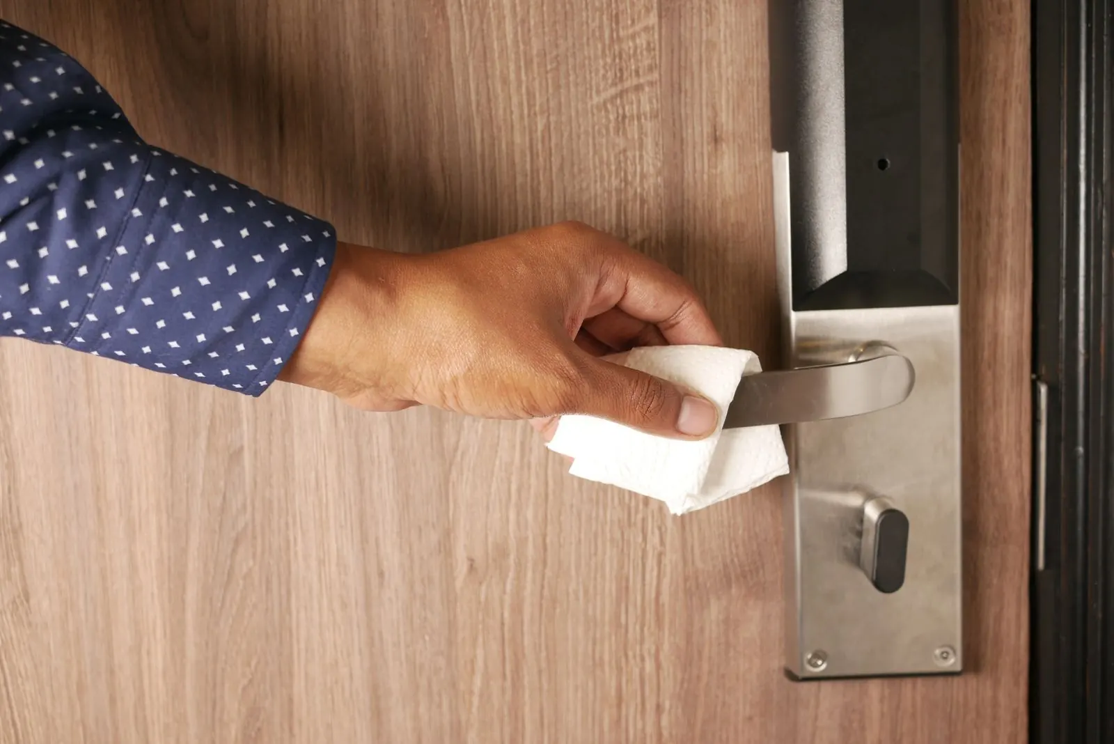 Cleaner disinfecting a door handle, one of the high-touch surfaces in a medical office