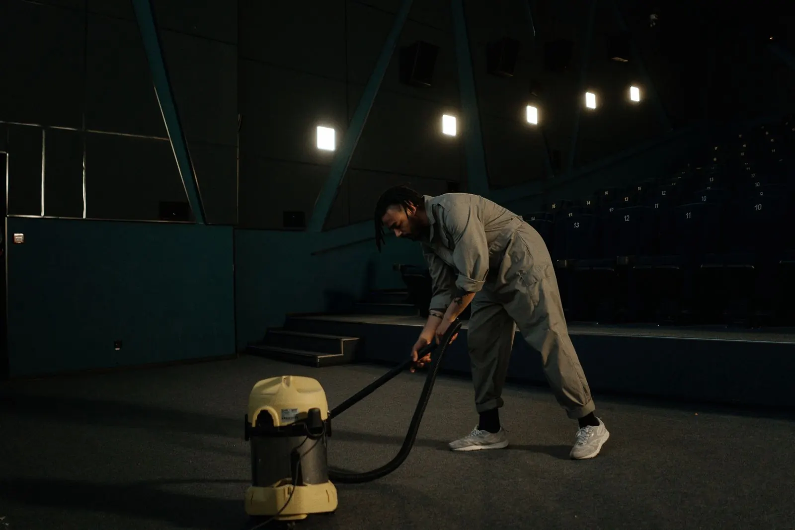 Janitorial crew member vacuuming the carpet of a dark auditorium after hours